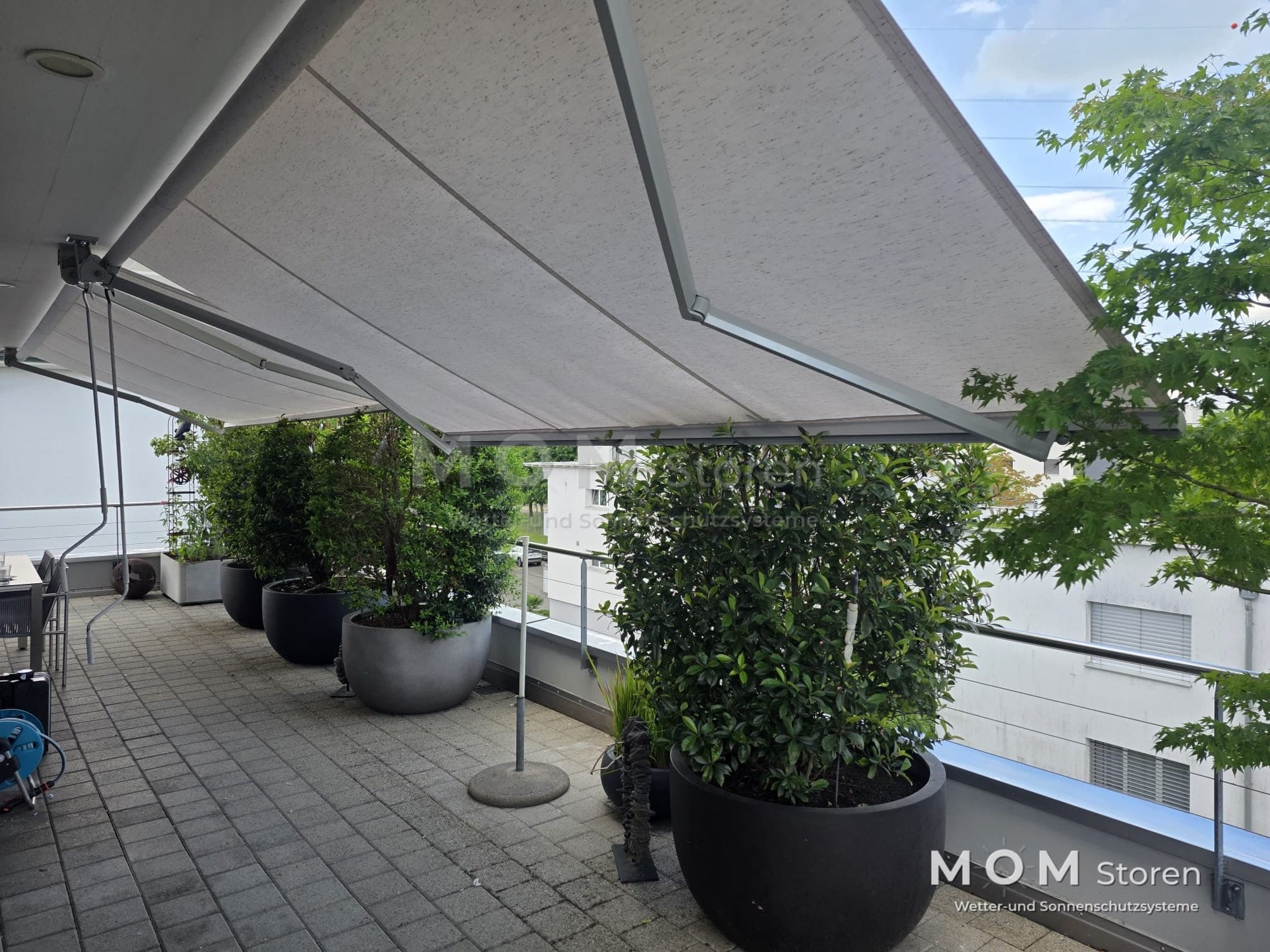 Grey folding-arm awning above a planted terrace