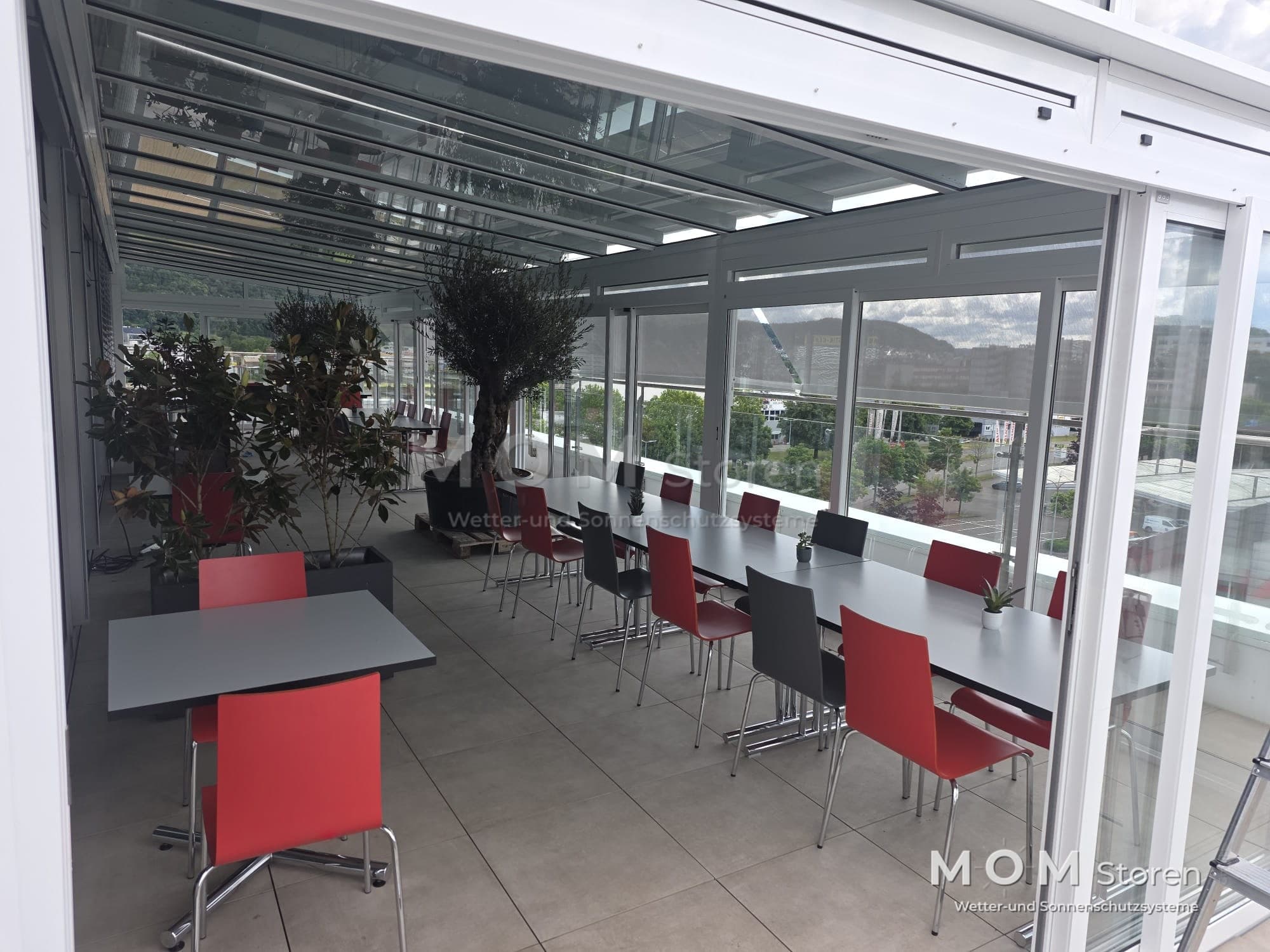 Glazed hospitality space with tables and red chairs